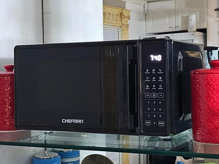 Black Chefman microwave on a glass shelf in a kitchen, featured in popular Cyber Monday deals this year.
