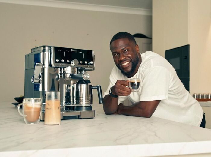 Man smiling with a coffee machine and drinks on a kitchen counter showcasing top Cyber Monday deals for coffee lovers.