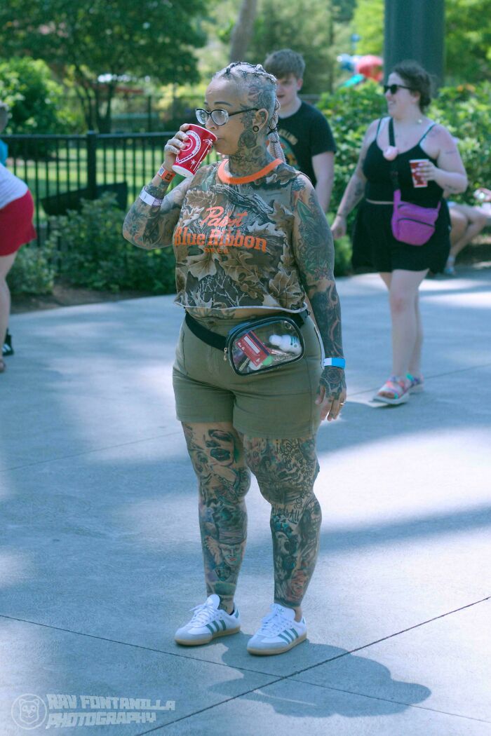 Woman with full-body tattoos drinking soda outdoors, showcasing human diversity and strength in a candid portrait.