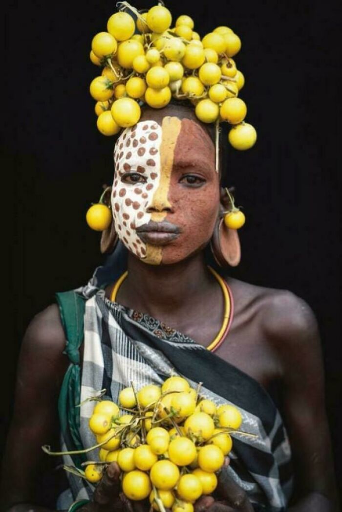 Portrait of a person with body paint and traditional headwear holding yellow fruits, capturing human beauty, strength, and diversity. Portrait of a person with body paint and traditional headwear holding yellow fruits, capturing human beauty, strength, and diversity.