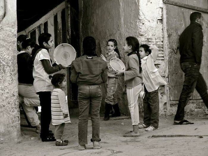 Group of children playing with tambourines in an urban setting, showcasing human diversity and strength in a candid portrait.
