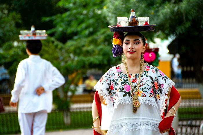 Young woman in traditional dress balancing a tray, showcasing the beauty, strength, and diversity of humans often overlooked