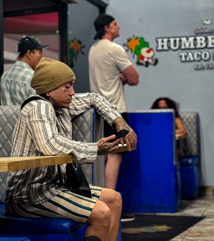 Young man with tattoos and a beanie sitting at a taco shop, capturing the beauty and diversity of overlooked humans.