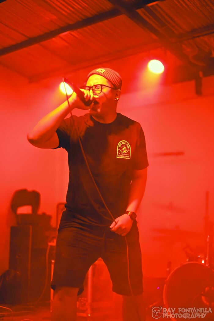 Man wearing glasses and a beanie performing on stage, showcasing the diversity and strength of humans in portraits.