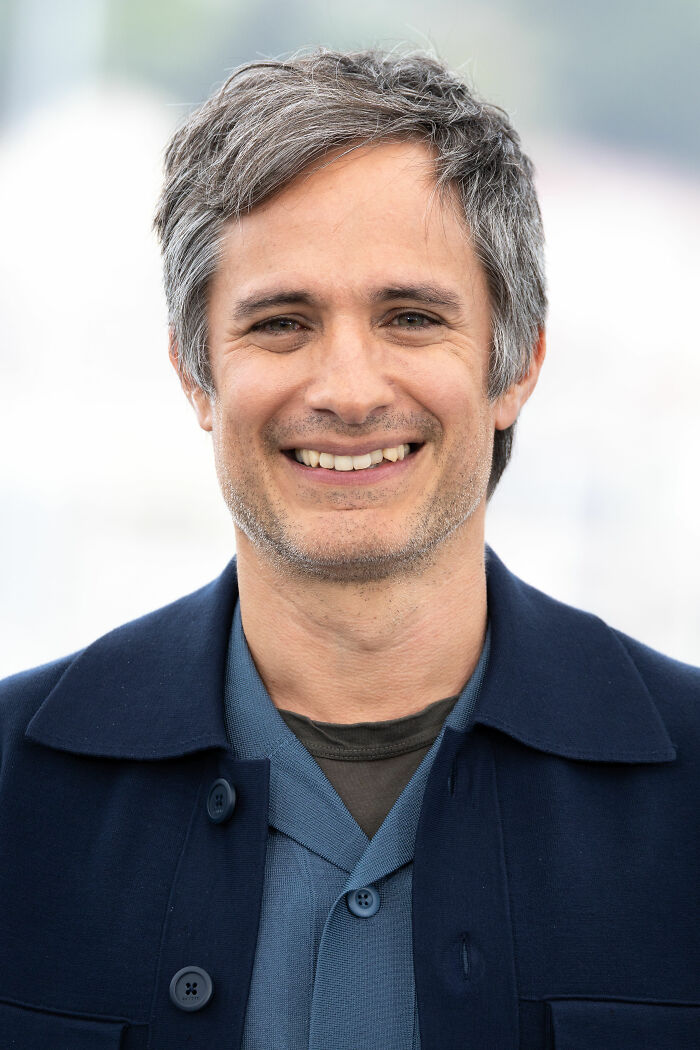 Gael García Bernal smiling outdoors, wearing layered shirts and a dark jacket, highlighting his bio and career.