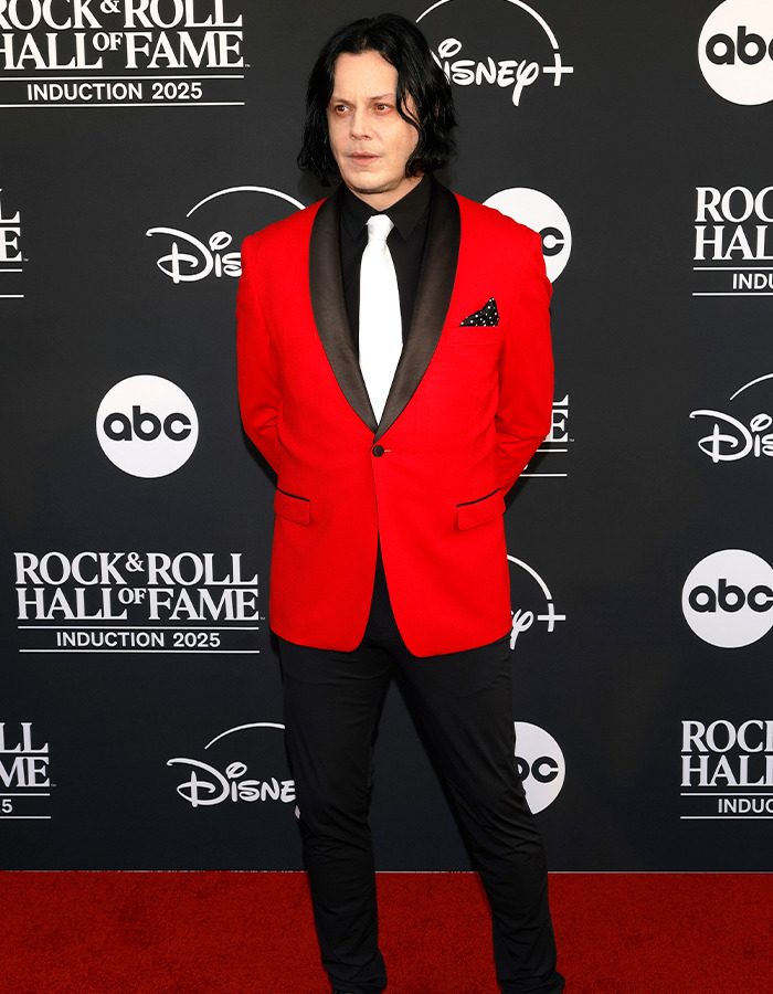 Person wearing a red blazer and white tie posing on the red carpet at the Rock Hall of Fame 2025 fashion event.