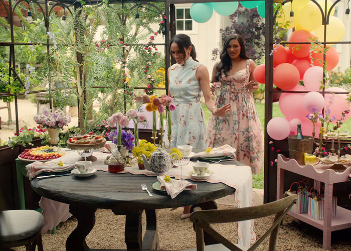 Meghan Markle in a floral dress at a festive garden party, creating a stylish Harper’s Bazaar moment.