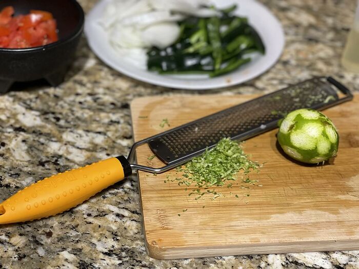 Zester and grater on wooden cutting board with fresh lime zest, fresh vegetables in background, kitchen finds.