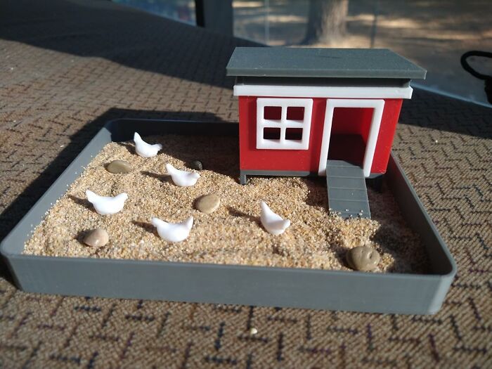 Miniature sandbox featuring a small red house and white chicken figures, a quirky novelty find for collectors.