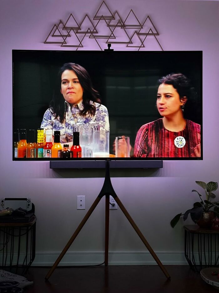 Two women having a conversation on a TV screen in a modern living room, illustrating Cyber Monday deals interest.