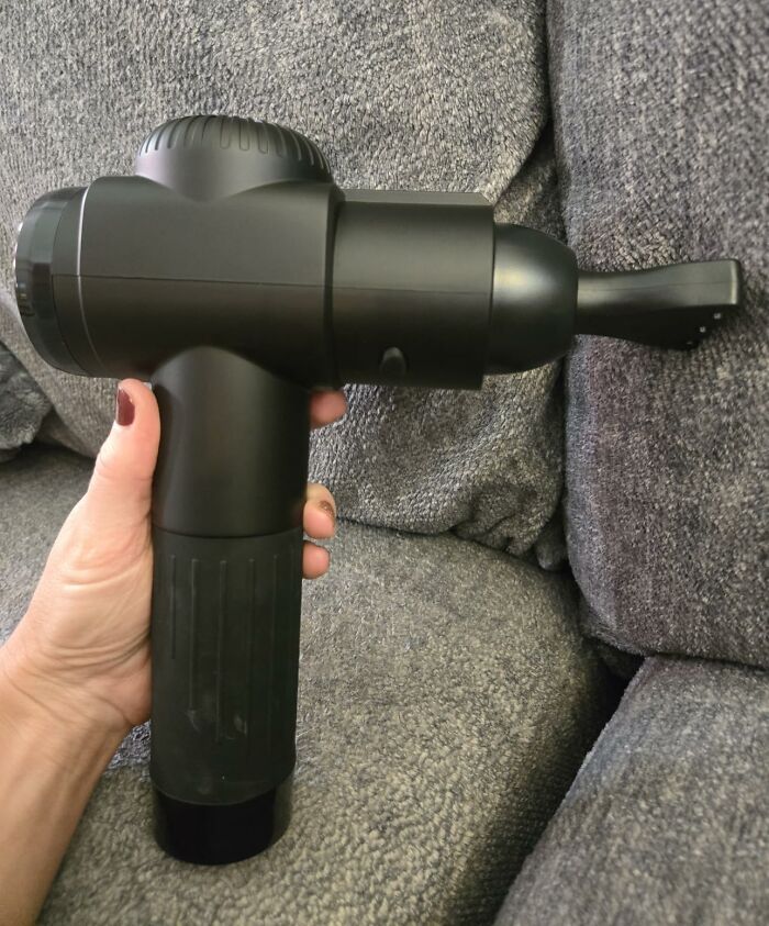 Hand holding a black massage gun device on a gray couch during Black Friday week hot deals event.