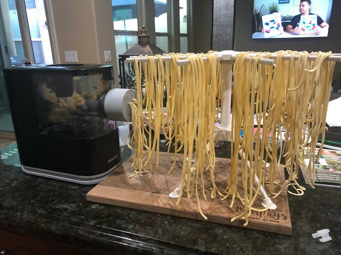 Homemade pasta noodles hanging to dry next to a pasta maker on a kitchen countertop, showcasing Black Friday deals.