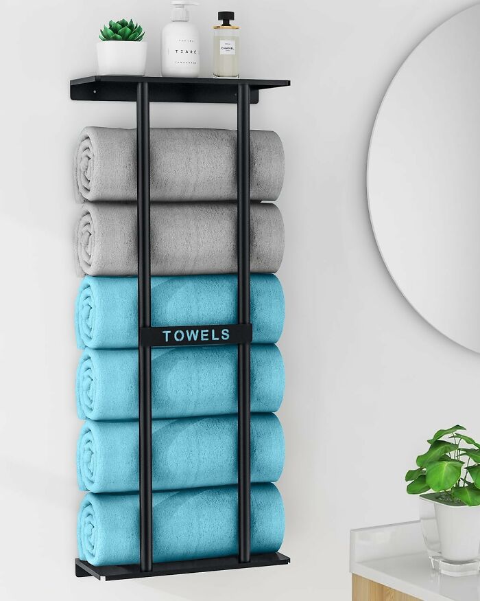Black wall towel rack holding rolled cozy blue and gray towels with decorative items, enhancing home comfort and style.