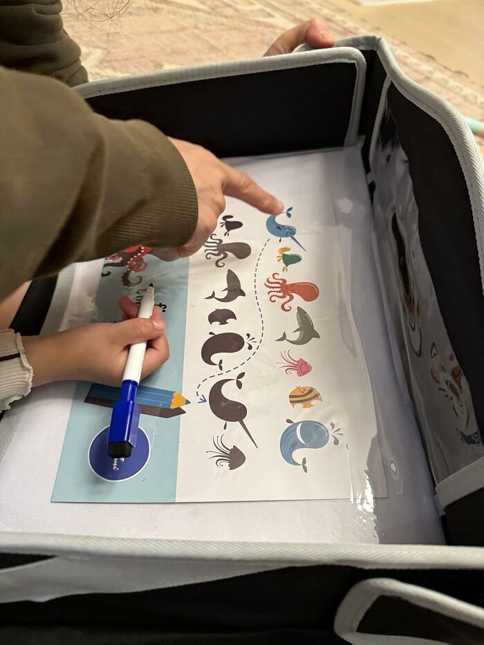 Adult pointing at sea animal illustrations on a Black Friday wishlist deal sheet held by a child with a blue marker.