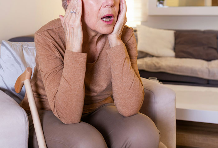 Older woman sitting on a couch, holding her face in shock, illustrating wildest family drama being shared online.