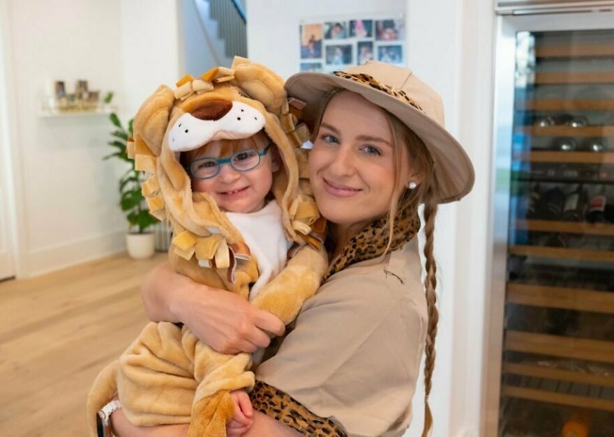 Meghan Trainor smiling and holding a child dressed in a lion costume in a bright, modern home setting. Meghan Trainor smiling and holding a child dressed in a lion costume in a bright, modern home setting.
