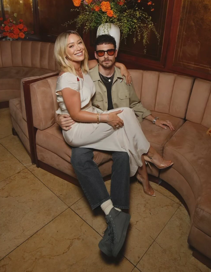 Hilary Duff and Joel Madden sitting together on a curved sofa, highlighting renewed outrage over their age-gap relationship.