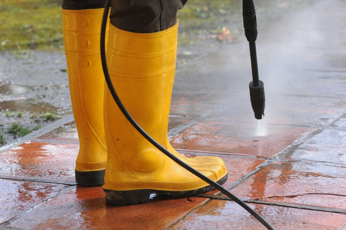 Person in yellow boots pressure washing a tiled patio, illustrating dummed HOA rules causing frustration with homeowners.