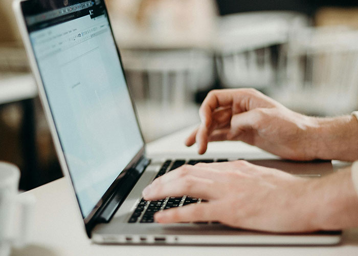 Person typing on laptop keyboard sharing life hacks in a bright workspace with blurred background.