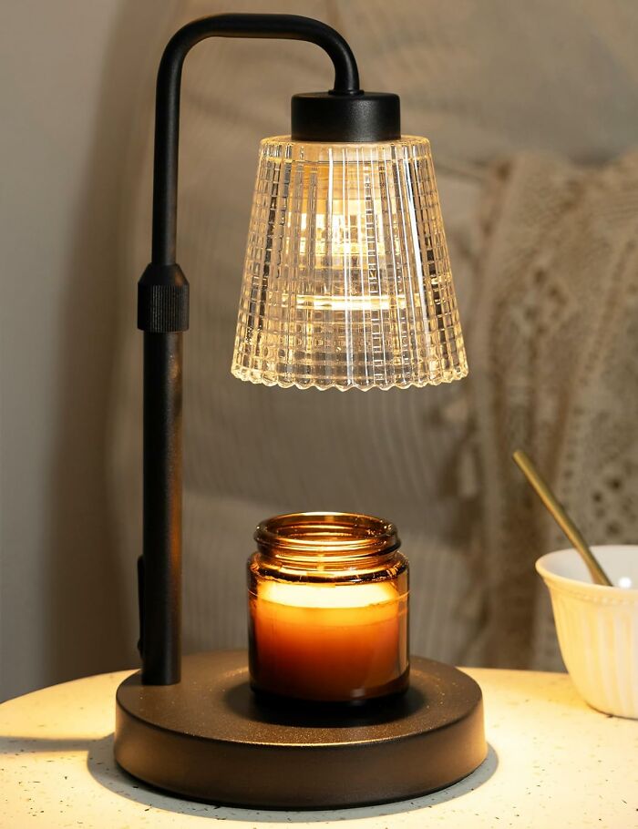 Black metal lamp with a textured glass shade and a glowing candle jar, creating a cozy home ambiance.