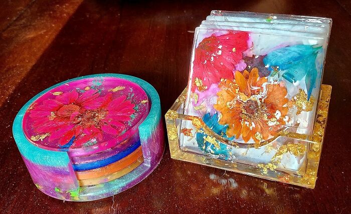 Colorful resin coasters with embedded flowers and gold flakes on a wooden surface, showcasing a creative hobby for hibernation season.