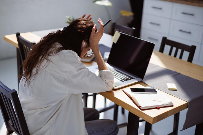 Stressed woman sitting at a desk with laptop and notebook, reflecting on lessons learned from past mistakes. Stressed woman sitting at a desk with laptop and notebook, reflecting on lessons learned from past mistakes.