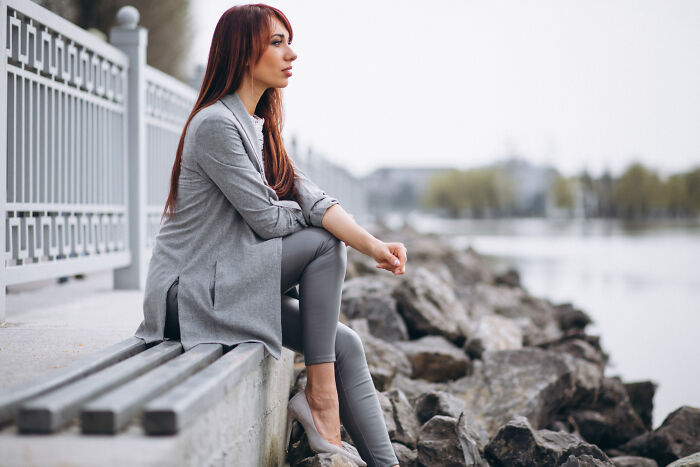 Young woman sitting by the water, reflecting quietly, representing people who disappeared to start new lives and reveal experiences.