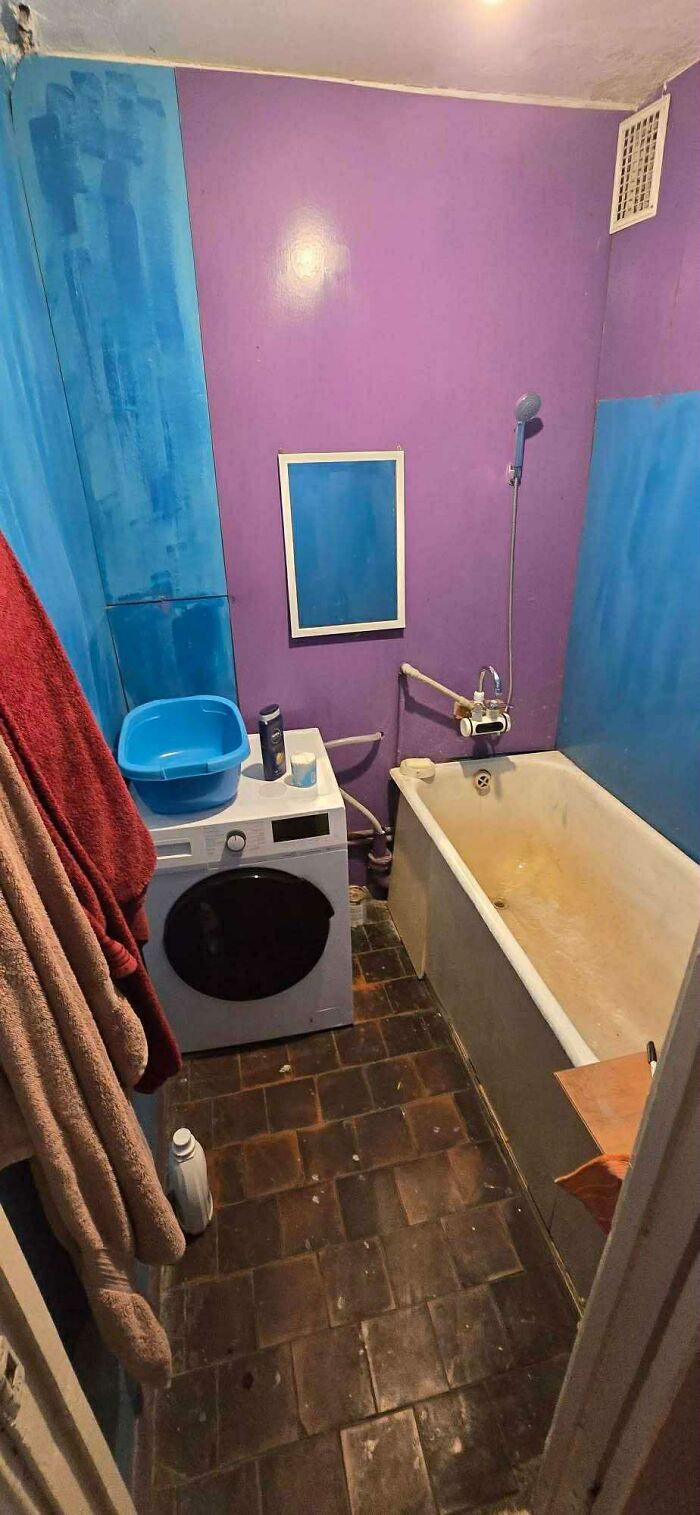 Small bathroom in a real estate listing with purple and blue walls, a washing machine, and a stained bathtub in poor condition.