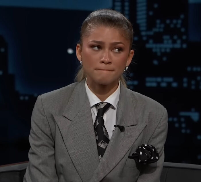 Zendaya in a gray suit and patterned tie, appearing thoughtful during a late night TV interview about petty feud controversies. Zendaya in a gray suit and patterned tie, appearing thoughtful during a late night TV interview about petty feud controversies.