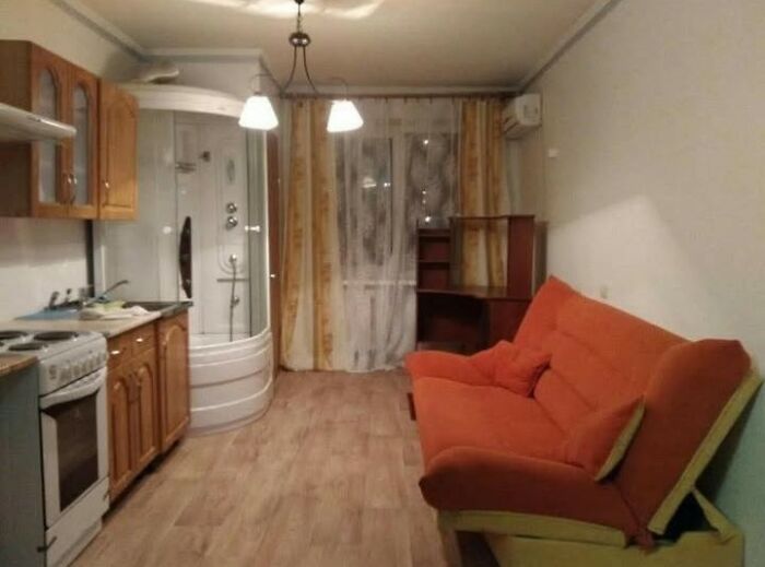 Small apartment interior with kitchen, shower cabin, and orange couch, an example of wild real estate listings.