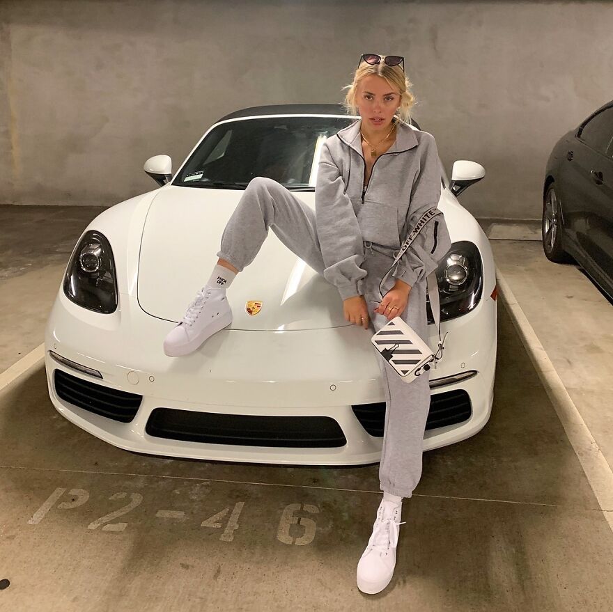 Corinna Kopf posing on a white Porsche in a gray tracksuit and white sneakers, showcasing internet fame net worth.