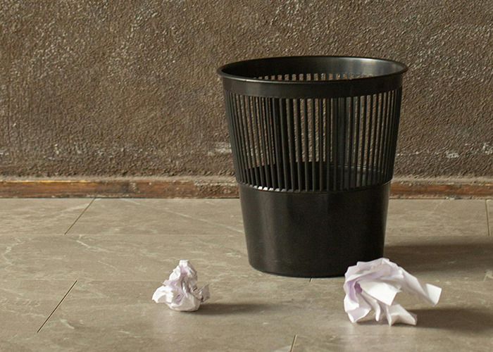 Black trash bin on floor with crumpled paper nearby, symbolizing horrible gifts people have actually received.