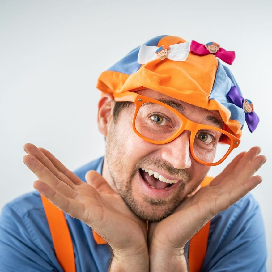 Man wearing colorful hat and orange glasses smiling enthusiastically, representing actors who have worn the Blippi bow tie. Man wearing colorful hat and orange glasses smiling enthusiastically, representing actors who have worn the Blippi bow tie.