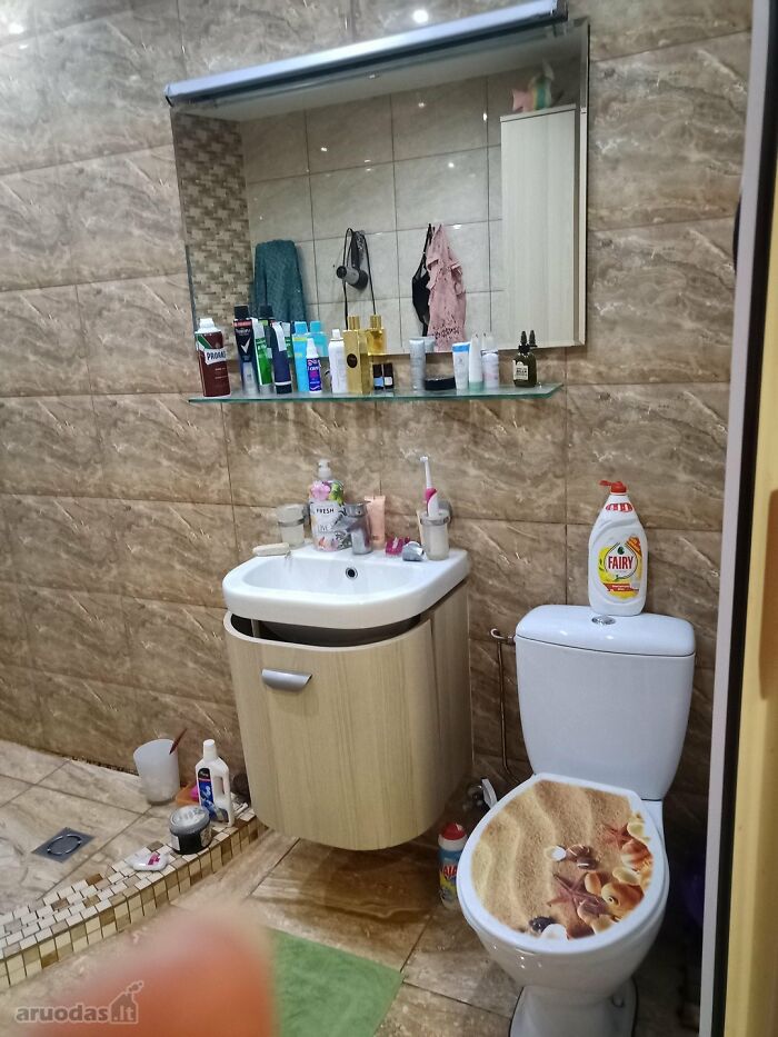Bathroom with cluttered sink, toilet with seashell seat cover, and various toiletries in a wild real estate listing photo.