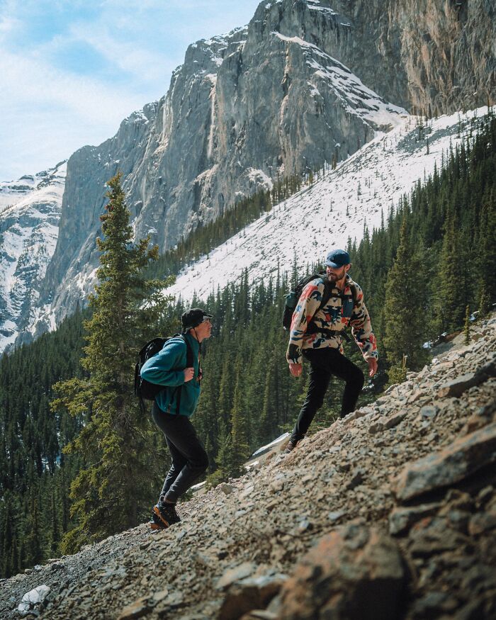 Two hikers climbing a rocky mountain trail surrounded by trees and snow, reflecting on purpose and life journey. Two hikers climbing a rocky mountain trail surrounded by trees and snow, reflecting on purpose and life journey.