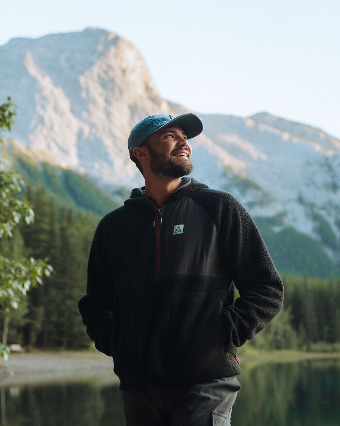 Man in outdoor jacket and cap smiling near lake with mountains, reflecting on purpose and personal journey in nature. Man in outdoor jacket and cap smiling near lake with mountains, reflecting on purpose and personal journey in nature.