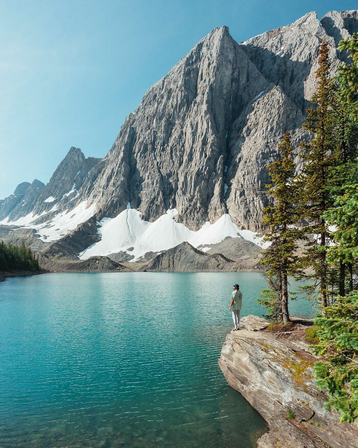 Person standing by a lake surrounded by mountains and trees, reflecting on purpose on a journey of self-discovery. Person standing by a lake surrounded by mountains and trees, reflecting on purpose on a journey of self-discovery.
