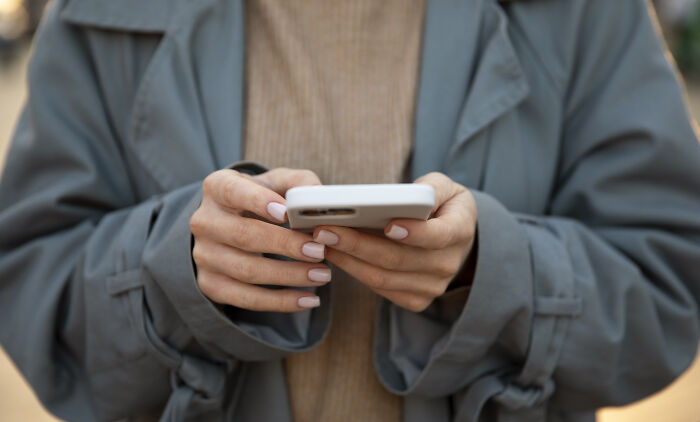 Person wearing a gray coat and beige sweater holding a smartphone, reflecting on a relationship with their brother after 20 years apart Person wearing a gray coat and beige sweater holding a smartphone, reflecting on a relationship with their brother after 20 years apart