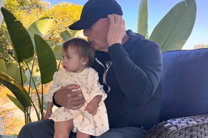 Bruce Willis sitting outdoors holding a young child, showing a tender moment amid his dementia journey update. Bruce Willis sitting outdoors holding a young child, showing a tender moment amid his dementia journey update.