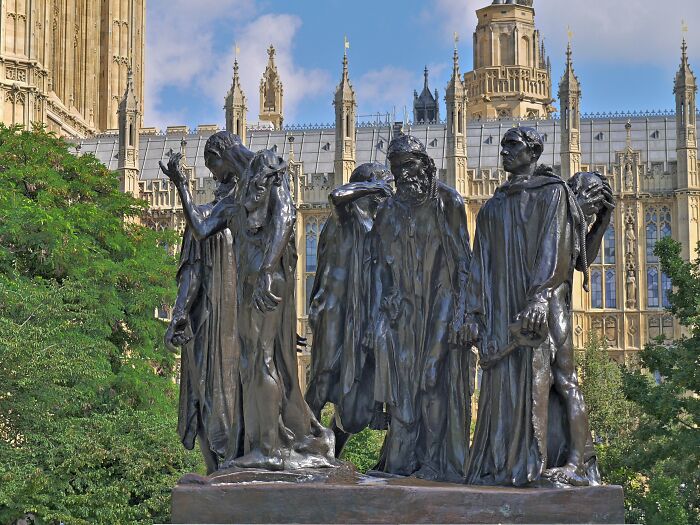 Bronze sculptures of somber figures displayed outdoors with historic Gothic architecture in the background, iconic travel bucket list.