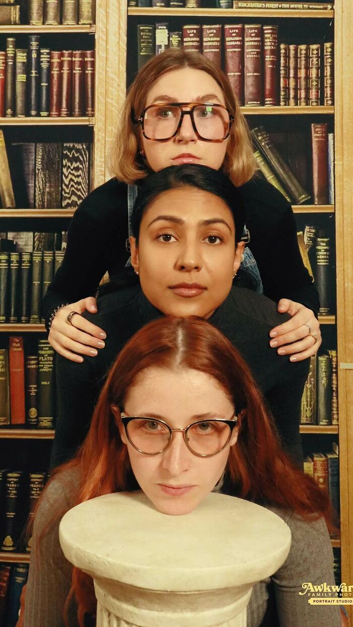 Three women stacked vertically in an awkward studio pose with a bookshelf backdrop, showcasing awkward studio pics humor.