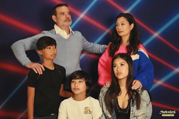 Family posing for awkward studio pics with retro laser background, capturing cringe-worthy and funny moments.