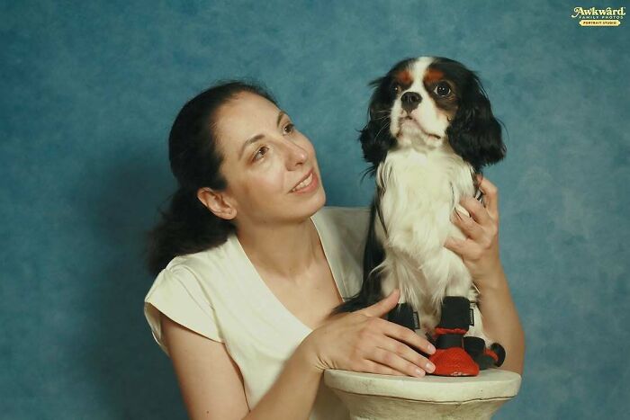 Woman posing with dog wearing red shoes in awkward studio pics with a blue background and neutral expressions.