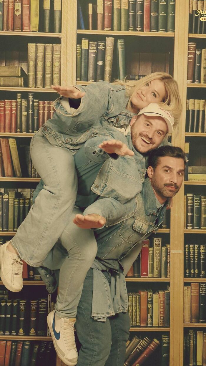 Three friends wearing denim outfits posing in an awkward studio picture with a bookshelf background and playful expressions.