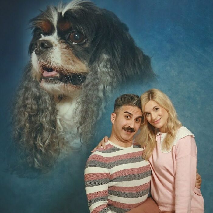 Couple posing with a large dog portrait in the background, creating a humorous and awkward studio photo setup.