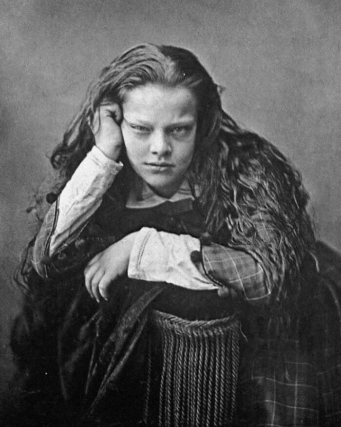 Victorian era black and white photo of a girl with long hair resting her head on her hand in a weird vintage portrait.