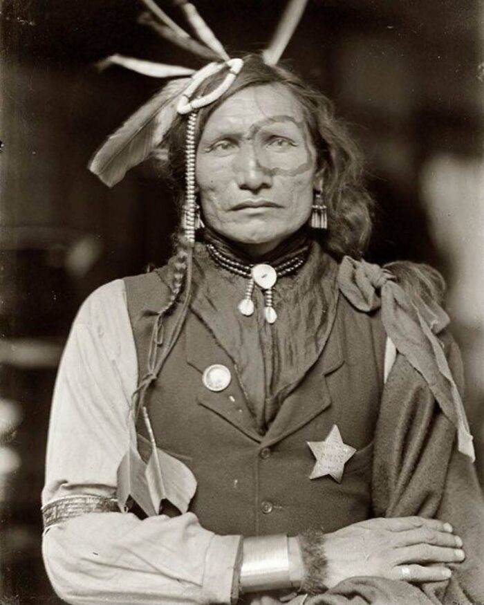 Victorian era portrait of a Native American man wearing traditional attire and a sheriff badge in a weird historic photo.