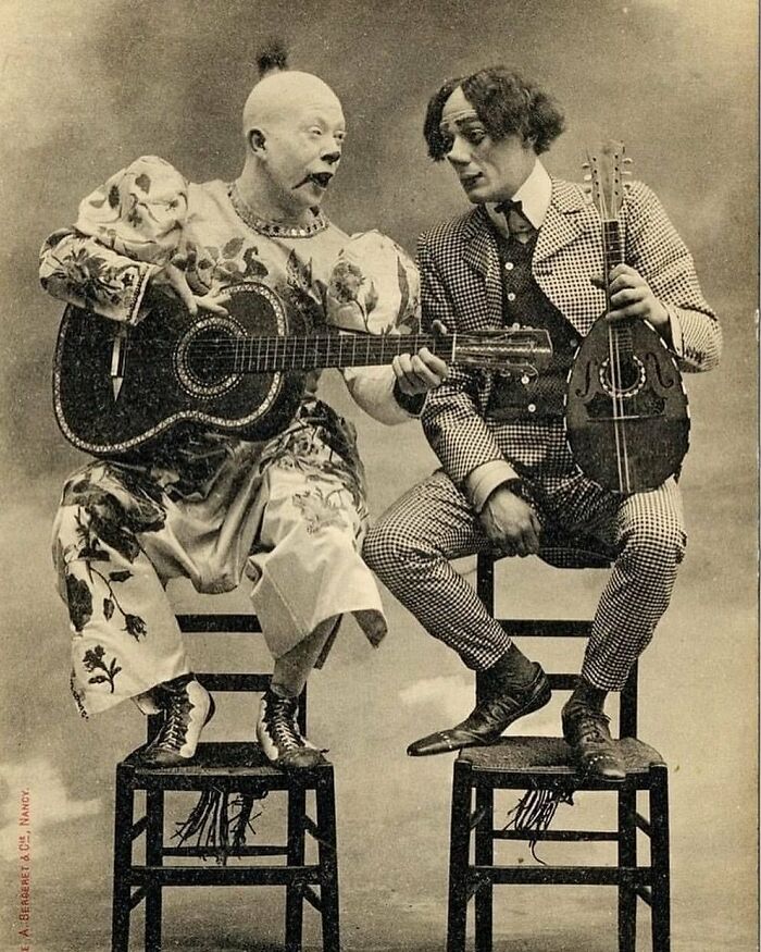 Two Victorian era performers in eccentric costumes, playing guitar and mandolin, showcasing weird photos from the era.