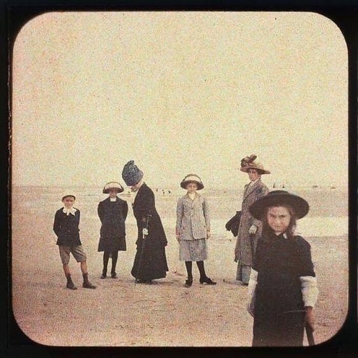 Group of Victorian era children and women wearing period clothing standing on a beach in a weird Victorian era photo.