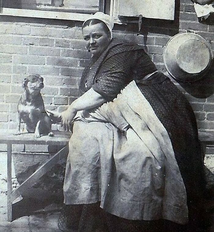 Victorian era woman in traditional dress sitting beside a dog on a bench in a black and white weird photo.